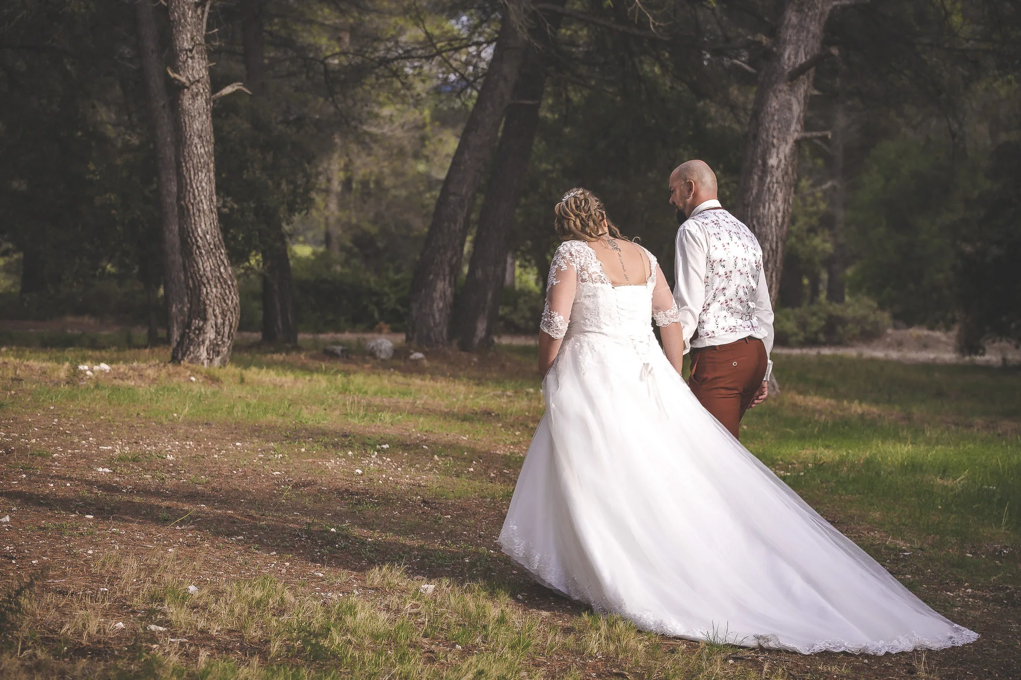 Les mariés marchant de dos, main dans la main, sous les pins d’un parc en Provence